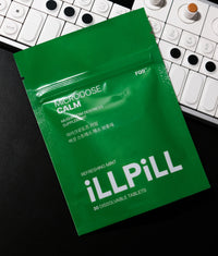 Lifestyle photo of an iLLPiLL MicroDose Calm 30-tablet green package on a dark surface with a music keyboard in the background